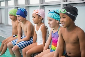 Young swimmers sitting poolside in swim caps